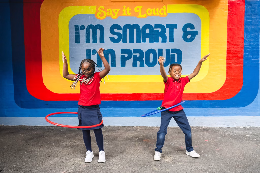 Children playing hullahop in front of a painted wall that says "I'm smart & I'm proud"